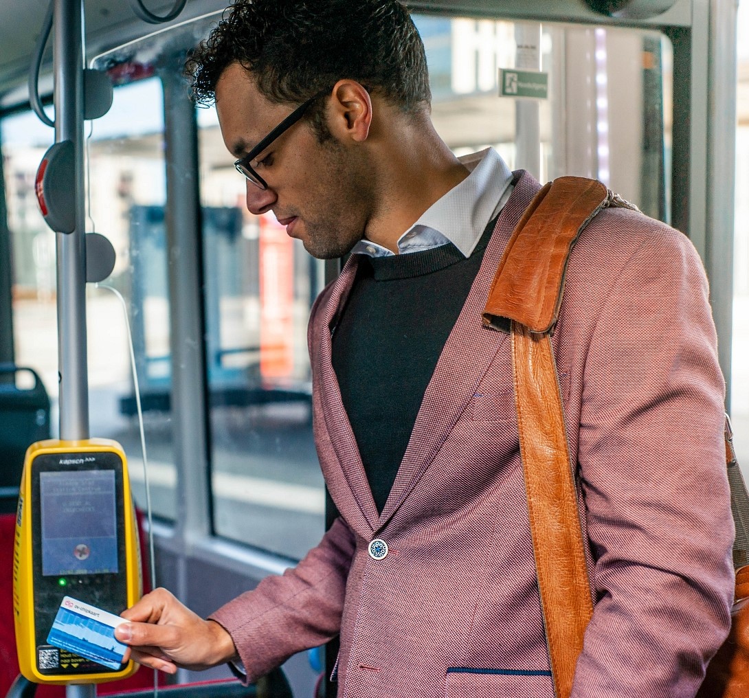 Mannelijke reiziger in kleurig pak en met schoudertas checkt in de bus in.